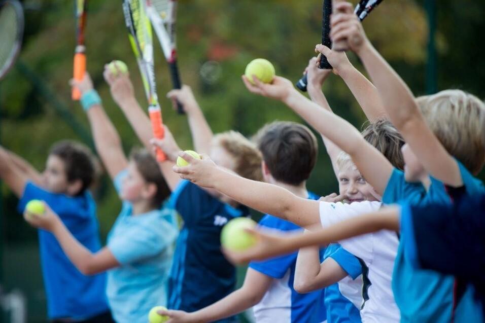 Gruppe von Kindern, die Tennisbälle hochwerfen, während sie Schläger in der Hand halten, auf einem Tennisplatz.
