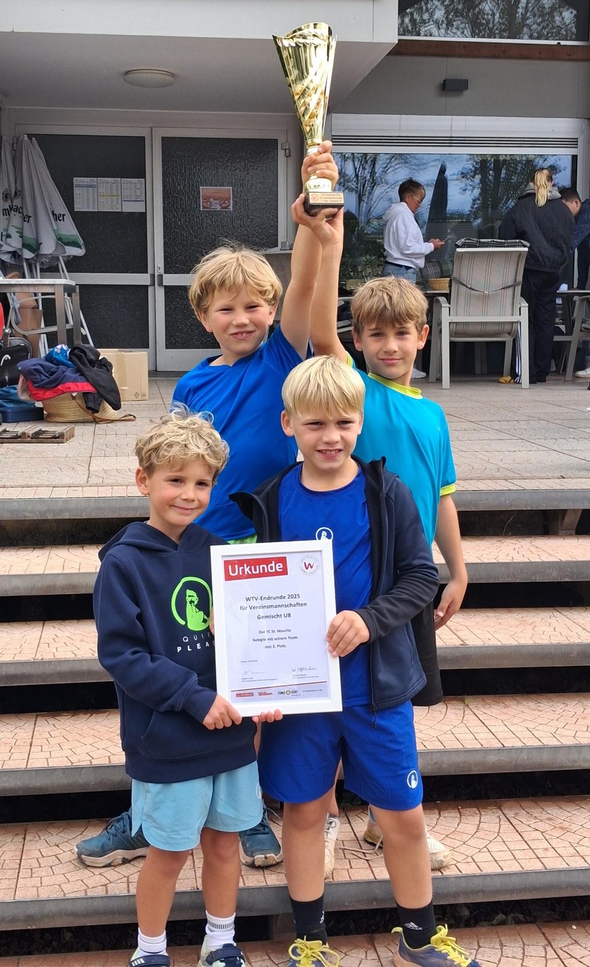 Vier Kinder stehen auf einer Treppe und halten einen Pokal und eine Urkunde in den Händen.