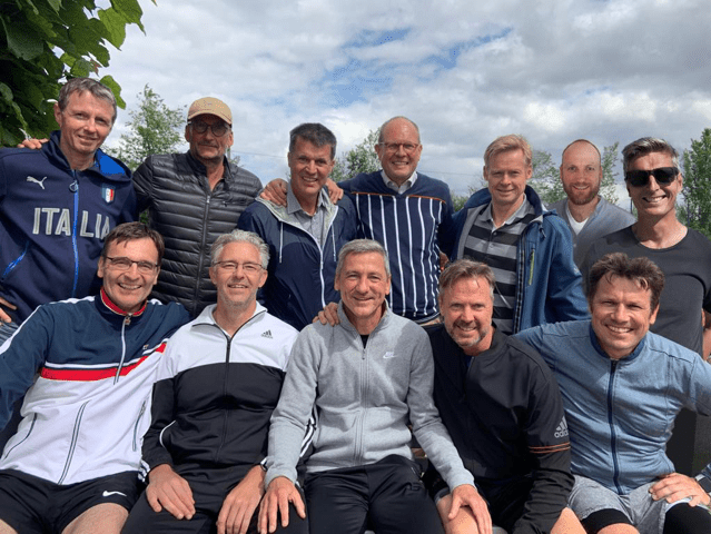 Gruppennahaufnahme von 12 Männern, lächelnd, im Freien vor bewölktem Himmel, in Sportkleidung.