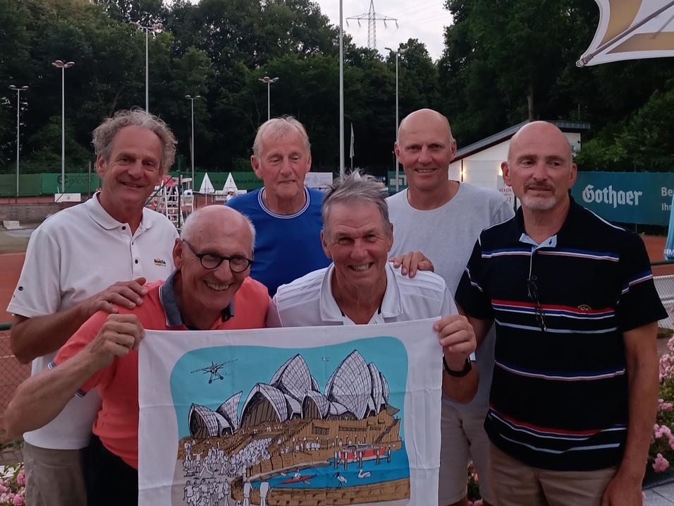 Sechs Männer posieren lächelnd auf einem Tennisplatz, halten ein buntes Bild mit bergigem Motiv in der Mitte.