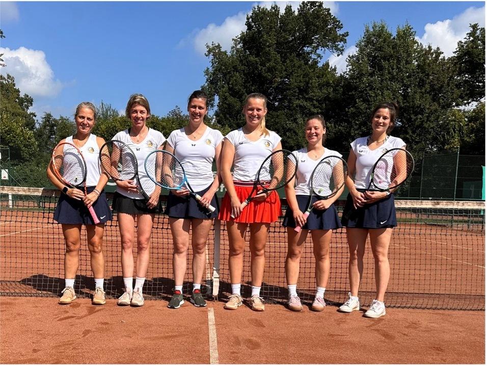 Sechs Tennisspielerinnen stehen lächelnd auf einem Sandplatz, jeweils mit einem Schläger in der Hand, im Hintergrund Bäume.