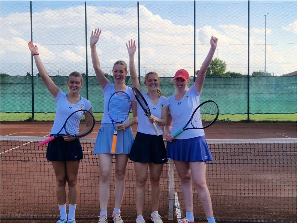 Vier junge Frauen in Tenniskleidung posieren auf einem Tennisplatz und halten Schläger in die Höhe.