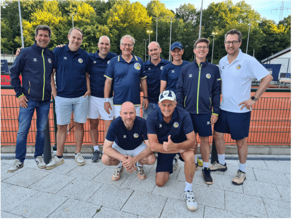 Zehn Personen in Sportbekleidung posieren lächelnd auf einem Tennisplatz mit grünen Bäumen im Hintergrund.