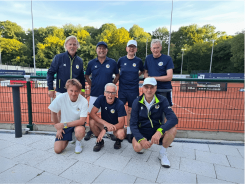 Gruppe von sechs Männern in Sportkleidung auf Tennisplatz, posierend vor grüner Landschaft und roten Plätzen.