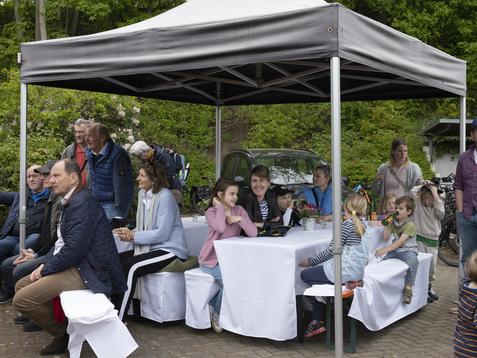 Menschen sitzen unter einem Pavillon, umgeben von Bäumen, während sie an Tischen entspannen.