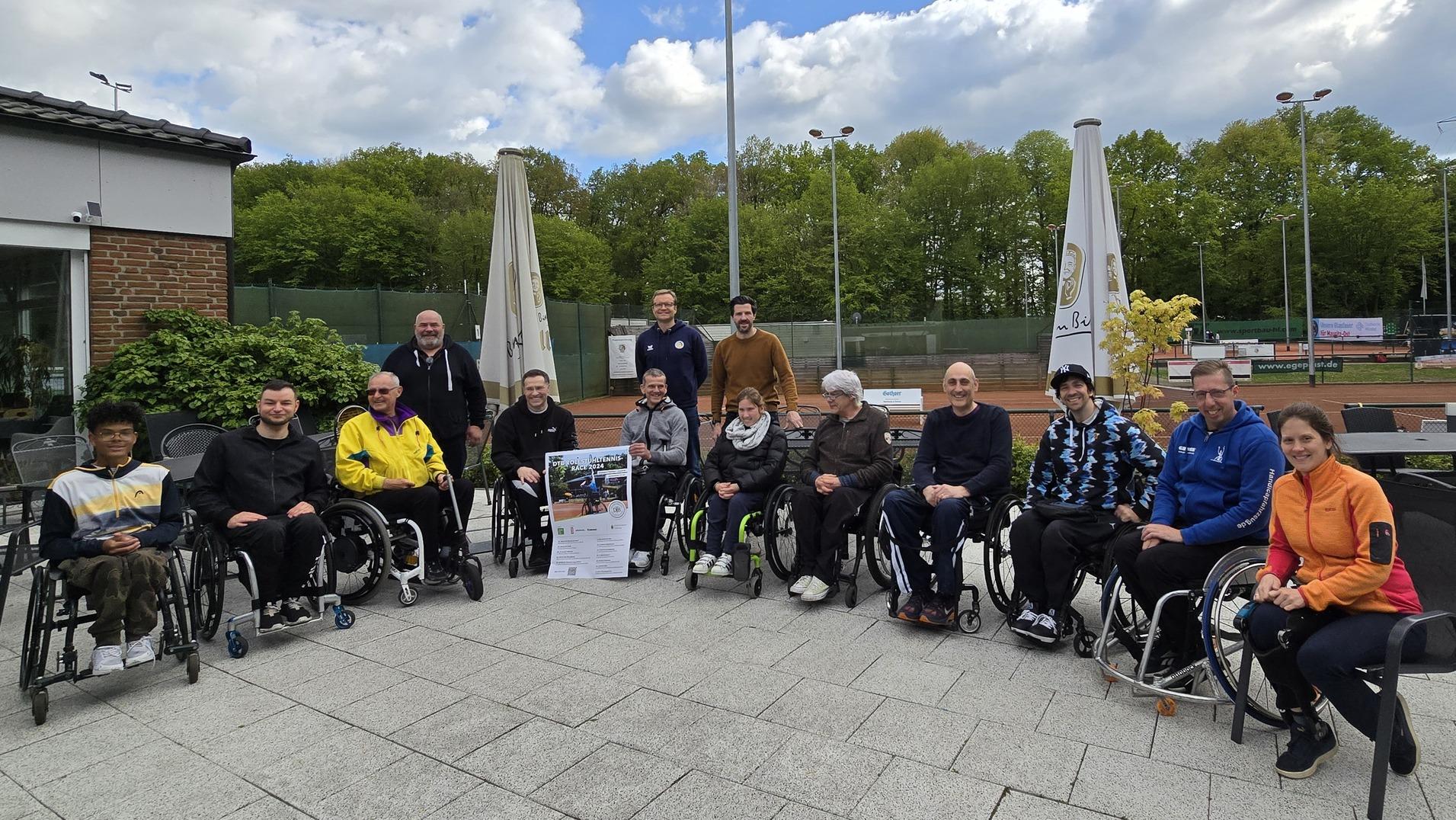 Gruppenaufnahme von 15 Personen im Rollstuhl, die vor einem Sportgelände auf einer Terrasse sitzen.
