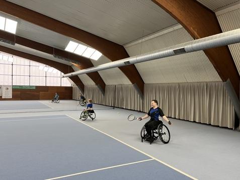 Rollstuhltennisspieler in einer Sporthalle, die auf einem blauen Platz Tennis spielen. Hintergründe mit Vorhängen.