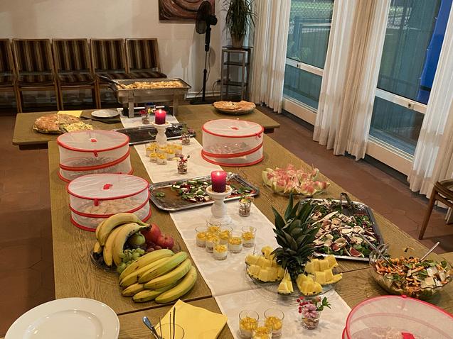 Buffet mit unterschiedlichen Speisen, Obst, Getränken und dekorativen Kerzen auf einem langen Tisch.