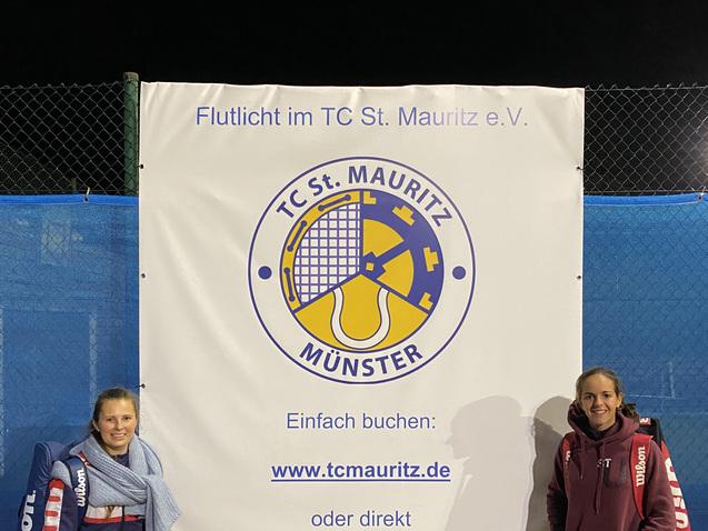 Zwei Tennisspielerinnen stehen neben einem Werbebanner des TC St. Mauritz in Münster.