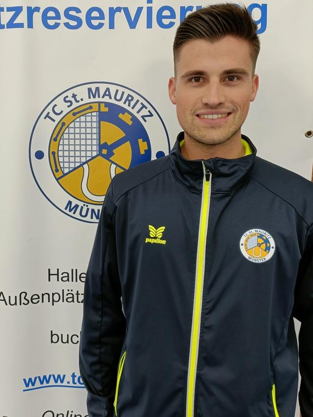 Lächelnder Mann in Sportjacke vor einem Banner mit dem Logo des TC St. Mauritz Münster und Informationen zur Platzreservierung.