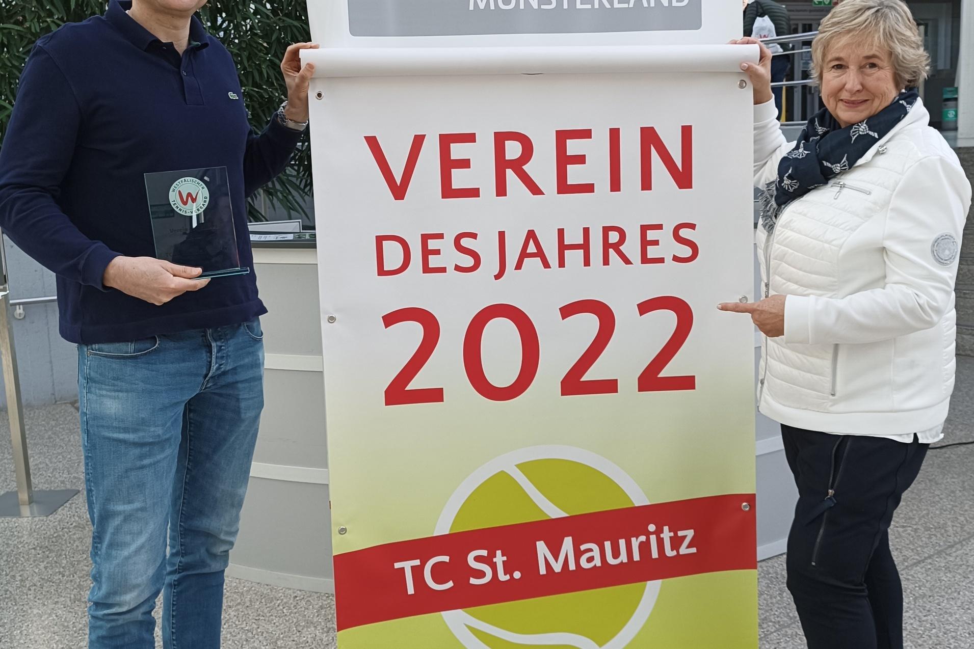 Zwei Personen präsentieren ein Banner mit der Aufschrift „Verein des Jahres 2022“ des TC St. Mauritz in einem Foyer.